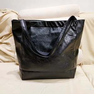 Gros plan sur le sac cabas noir en cuir huilé vintage avec poche sur canapé beige