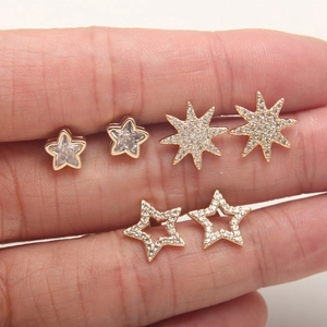 Three gold star stud earrings with cubic zirconia set on a person's finger for size