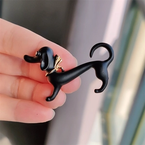Creative black dachshund enamel pin with gold bow held by hand for detailed view