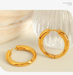 Detailed view of polished gold hoop earrings with fine hinge clasp on textured background
