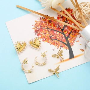 Detailed view of heart, star, and dragonfly gold earrings with pearls on decorative card