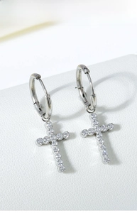 Macro shot of silver titanium cross earrings with zircon stones on white leather