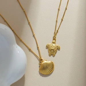 Detail of gold-plated bead necklaces with shell and sea turtle pendants on leather surface