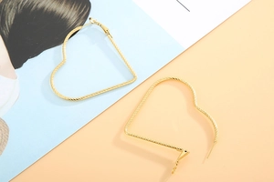 Macro detail of gold-tone heart hoop earrings featuring a sophisticated ribbed texture