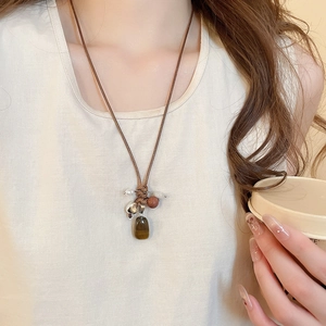 Detail of a brown woven rope necklace featuring a dark brown stone pendant and metallic beads