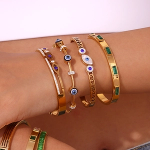 Close-up of gold evil eye beaded bracelet and green gemstone cuff on a model's wrist