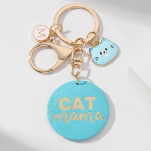 Porte-clés doré CAT MAMA avec breloques en émail bleu et initiale M rose sur fond gris