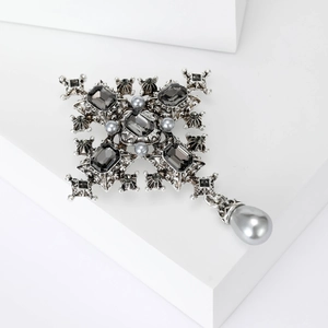 Baroque silver cross brooch with dark grey crystals and hanging pearl on a white pedestal