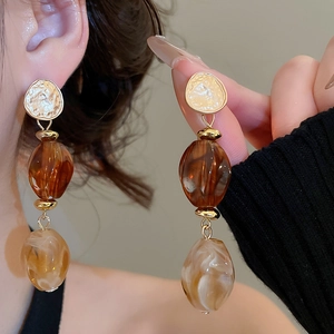 Detail of amber acrylic drop earrings with gold metal and marble resin beads on a model