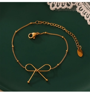 Detail of a gold-plated bow bracelet with adjustable lobster clasp on a green plate