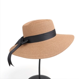 Elegant wide brim straw hat with black bow ribbon on a stand for sun protection