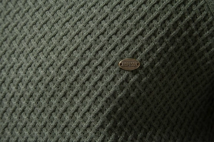 Close-up of deep army green cotton sweater featuring textured diamond knit and metal logo tag