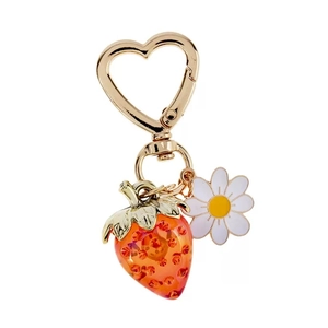 Close-up of heart-shaped gold clasp with strawberry pendant and daisy flower charm