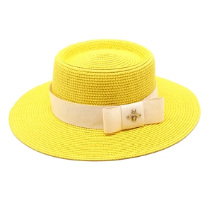 Detail of yellow straw hat featuring a beige ribbon and a golden metal bee ornament