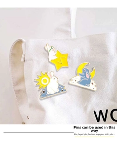 Detail view of cartoon rabbit enamel pins with sun moon and stars on a white canvas bag
