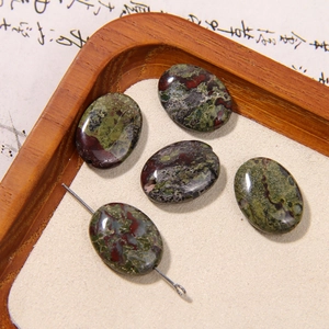 Close-up of five oval natural stone beads with red and green textures on a wooden tray