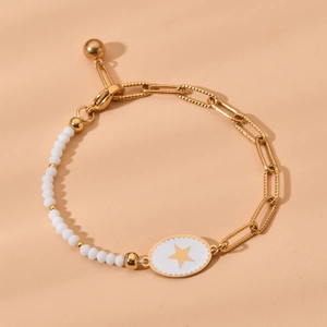 Gold paperclip chain bracelet with white beads and a star charm on beige background