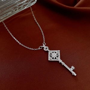 Detailed view of silver key pendant with zircon inlays on a dark satin background