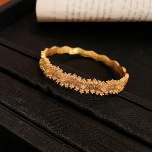 Detailed close-up of a gold wave bracelet with sparkling zircon rows on a gift box