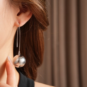Détail d'une boucle d'oreille argentée à texture brossée portée par un mannequin
