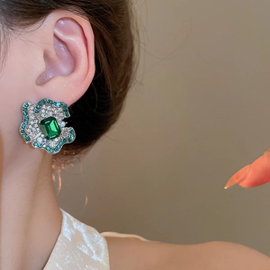 Close-up of luxury flower stud earring featuring a large emerald-cut green gemstone