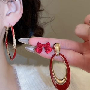 Detail of red enamel bow stud and gold geometric drop earrings on model's ear