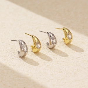 Macro shot of minimalist C-shape metal stud earrings with oval crystals in gold and silver