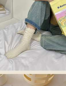 Detail of cream white ribbed slouch socks featuring a retro side label and frilly edges