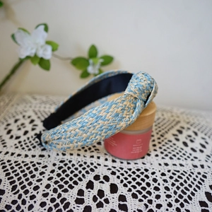Detail of blue and beige woven raffia headband with knot on white lace fabric