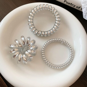 Three silver spiral telephone wire hair ties in a white ceramic dish on a wood desk