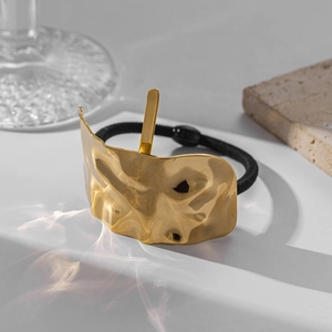 Detailed view of the gold irregular metal buckle and black elastic hair tie on a white surface