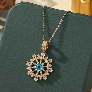 Detail of gold Evil Eye necklace with blue enamel and white zircons on a green case