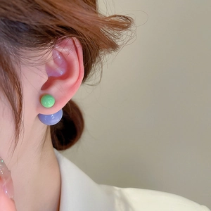 Detail shot of green and lilac spherical layered earrings worn on a female model's ear