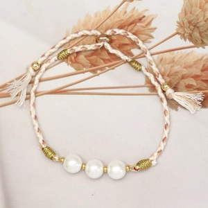 Close-up of woven bracelet featuring three white pearls and elegant gold thread accents
