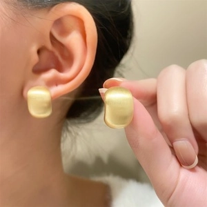 Detailed view of matte gold wide C-shaped hoop earrings worn and held for size guide