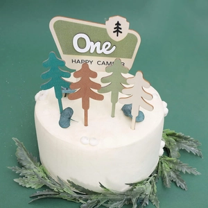 Detail of wooden One Happy Camper cake topper set with various pine tree shapes on white cake