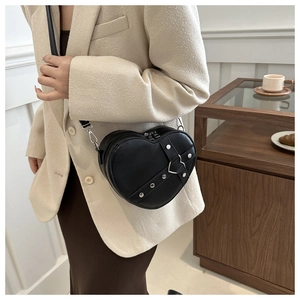 Détail d'un sac bandoulière noir en forme de cœur avec des rivets argentés et boucle