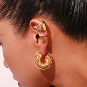 Detailed view of hollow gold-plated twisted earrings and pearl ear cuffs on model's ear