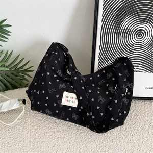 Detail der schwarzen Cord-Schultertasche mit weißem Herz- und Schleifendruck und breitem Gurt