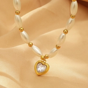 Detail of heart crystal pendant on gold pearl necklace over champagne silk background
