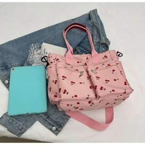 Detailed shot of pink tote bag with cherry print, showing front pockets and straps