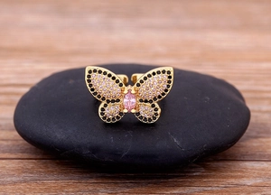 Detail of 18K gold butterfly ring with pink and black crystals on dark stone
