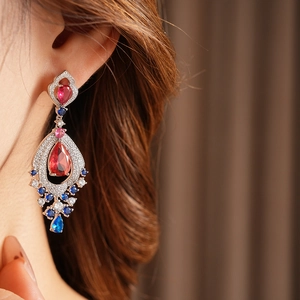 Close-up of vintage teardrop earrings with red and blue stones worn by a model