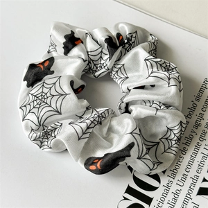 Detail of white satin Halloween scrunchie featuring black spider webs and ghost patterns
