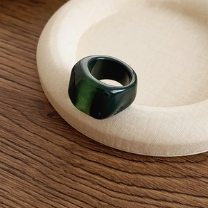 Detailed close-up of a thick dark green resin ring displayed on a minimal beige plate