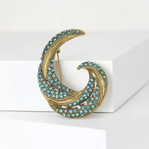 Detail of vintage bronze crescent brooch with pale blue crystals on white geometric stand