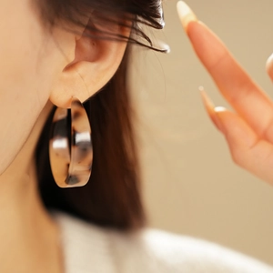 Close-up of minimalist brown tortoiseshell resin C-shaped hoop earrings on model ear