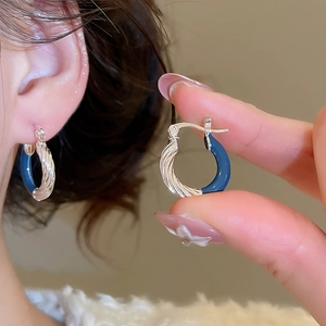 Detailed close-up of silver textured hoop earrings with deep blue enamel and spiral pattern