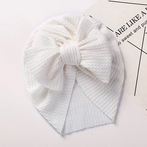 Detail of white baby beanie featuring waffle texture and large bow decoration