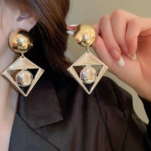 Close-up of golden geometric diamond earrings with round bead drop on a model